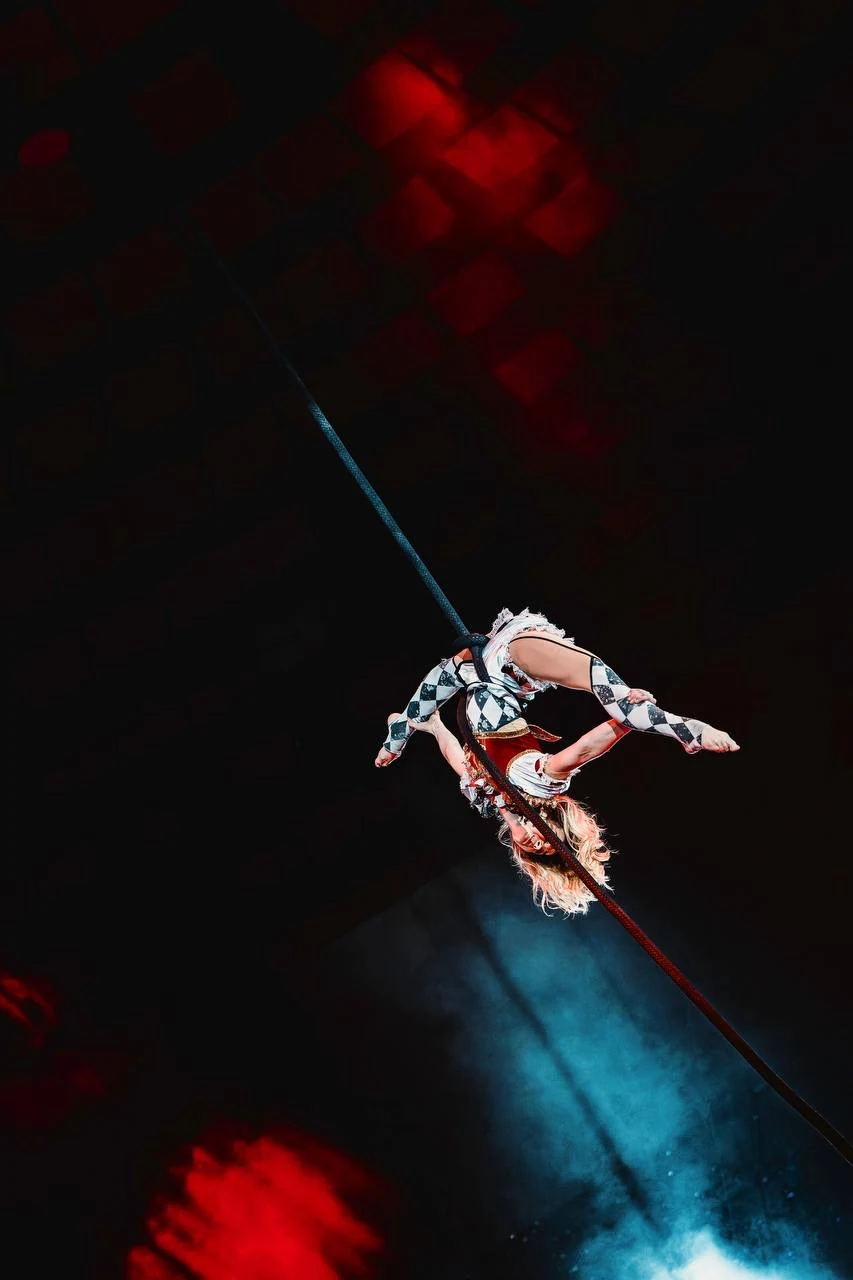 A gymnast performing on corde de péril in red and blue stage lighting